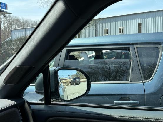 A picture of a live duck (confirmed) in the backseat of a car. The picture is through the window of my car. In my rearview mirror is another car and a sign for Landry in Westborough, Massachusetts.