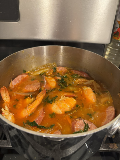 Pot of kimchi jjigae with shrimp and sliced sausages. The broth is fiery red. 