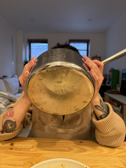Person with tattooed forearms drinking soup straight from the pot