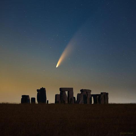 Comet stretching across a star-filled evening sky over a prehistoric ring of stones.