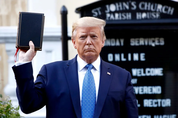 President Trump standing outside, holding a black bible upside down. 