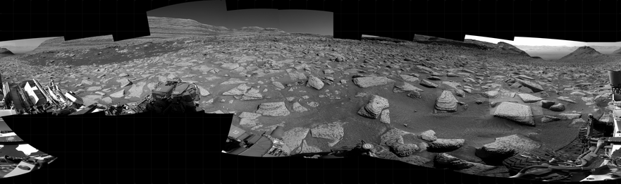 A black and white mosaic capturing a Martian landscape. In detail, NASA's Mars rover Curiosity took 22 images in Gale Crater using its mast-mounted Right Navigation Camera (Navcam) to create this mosaic. The seam-corrected mosaic provides a 360-degree cylindrical projection panorama of the Martian surface centered at 202 degrees azimuth (measured clockwise from north). Curiosity took the images on April 16, 2025, Sol 4512 of the Mars Science Laboratory mission at drive 960, site number 115. The local mean solar time for the image exposures was from 2 PM to 3 PM. Each Navcam image has a 45 degree field of view. 