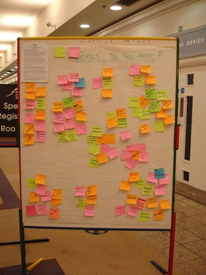 what attendees want to talk about: a photograph of a portable cork board covered with flipchart paper containing many different written sticky notes. Photo attribution: Flickr user edmittance