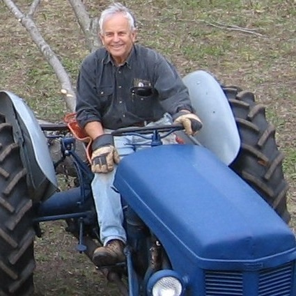 My smiling father astride his vintage 1950's tractor dragging cut branches from working at maintaining our sugar maple grove.