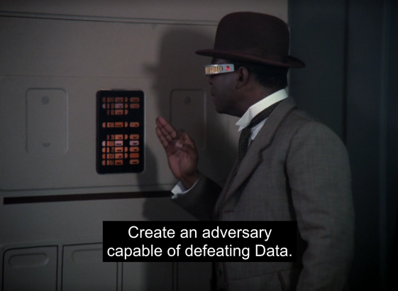 This image shows Geordi La Forge from the *Star Trek: The Next Generation* episode "Elementary, Dear Data." He is dressed in a Victorian-era suit and bowler hat as part of a holodeck simulation based on Sherlock Holmes stories. Geordi is facing a wall-mounted control panel with illuminated orange buttons, issuing a command. He wears his iconic VISOR, which allows him to see despite being blind. The subtitle reads, “Create an adversary capable of defeating Data,” marking a pivotal moment in the episode when Geordi inadvertently triggers the creation of a self-aware holodeck character, leading to unexpected consequences.