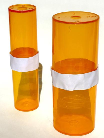 two large and two small orange prescription medication containers are joined opening to opening by a white strip of material. two oblong, cylindrical, translucent containers are the result.