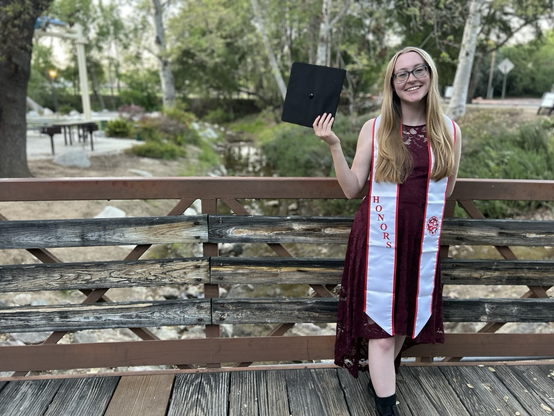 Teagan wearing her CSUN honors sash and holding a graduation cap in her right hand.