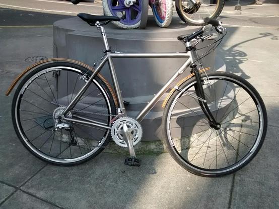 My bicycle, a raw titanium silver color, leaning on a gray cement structure. Looks like a lot of bicycles, most notable might be the wooden fenders.