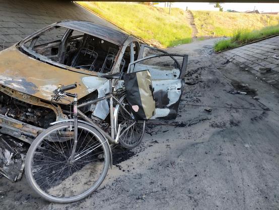 my bike leaning against a burned out car which was abandoned on a pedestrian multi use path.