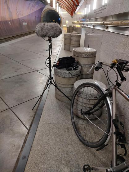 My bike leaning against a wall in an underground train station with a microphone on a stand which is recording the ambient sound of the station.