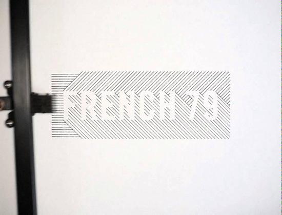 screenshot of the video, a plotter draws text with a black pen on white canvas saying "FRENCH 79"