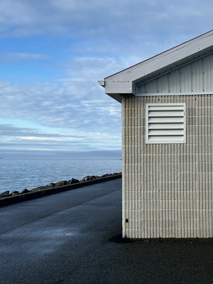 A photography of a building next to the sea, with a cloudy sky. The composition is balanced.