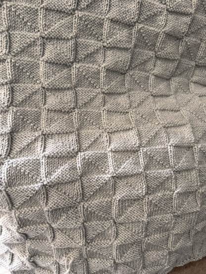 Eine selbstgestrickte hellgraue Decke 