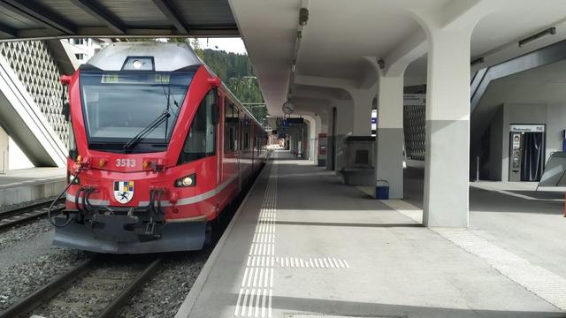 Triebwagen der Rhätischen Bahn der Strecke Chur-Arosa im typischen Rot der Gesellschaft im Bahnhof Arosa, abfahrbereit in Richtung Chur. Auch im Bild das Betondach des Bahnsteigs 1 und links die Treppe der Fußgängerüberführung über die Gleise, die auch zur Luftseilbahn 'Weißhornbahn' führt.