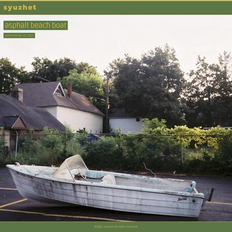 A photo of a battered, two-seat boat is placed in a parking spot in an empty parking lot. Bushes overtake a tired barbed wire fence in the background. 