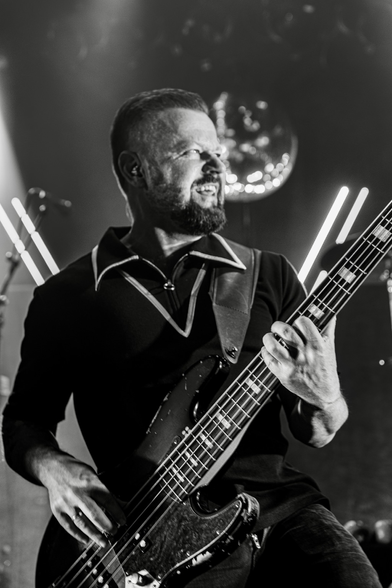 Bearded man playing bass guitar live on stage - lights and a disco ball in background- picture is B/W