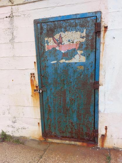 .. front on pic of a blue iron door in a whitewashed [❗️] rust spotted stonewall .. top half of door has a frayed cartoon of the eponymous animated .. um .. "icon" .. ❗️☝️