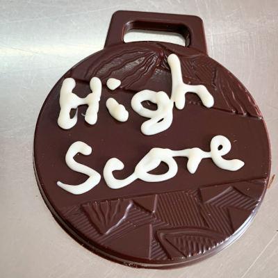 Eine Medaille aus dunkler Schokolade. Darauf steht in Weißer Schokolade „Highscore".