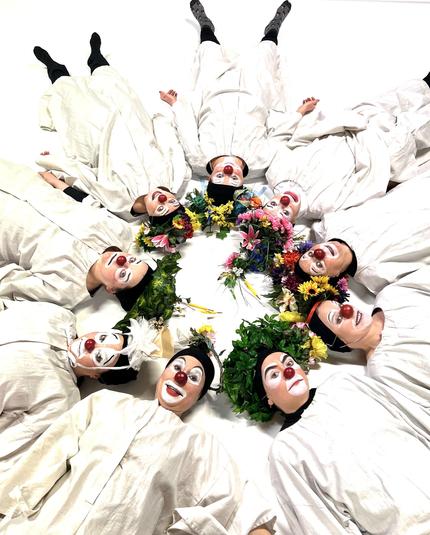 Clown choir members in their angelic robes and flower wreaths are laying on the ground in a circle.
