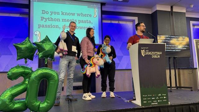 DjangoCon Europe 2025 Conference stage picture with 3 hosts grabbing one unicorn balloon each. And a speaker. 