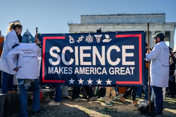 A very large poster saying "SCIENCE MAKES AMERICA GREAT" held by scientists in white coats in front of a federal building in Washington, DC. during a March 9, 2025 protest. Photo by Geoff Livingston.