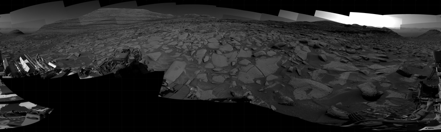 A black and white mosaic capturing a Martian landscape. In detail, NASA's Mars rover Curiosity took 31 images in Gale Crater using its mast-mounted Right Navigation Camera (Navcam) to create this mosaic. The seam-corrected mosaic provides a 360-degree cylindrical projection panorama of the Martian surface centered at 191 degrees azimuth (measured clockwise from north). Curiosity took the images on April 18, 2025, Sol 4514 of the Mars Science Laboratory mission at drive 1320, site number 115. The local mean solar time for the image exposures was from 2 PM to 3 PM. Each Navcam image has a 45 degree field of view.