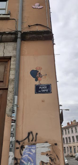 Street artiste au dessus du nom de la rue : Place des Tapis 