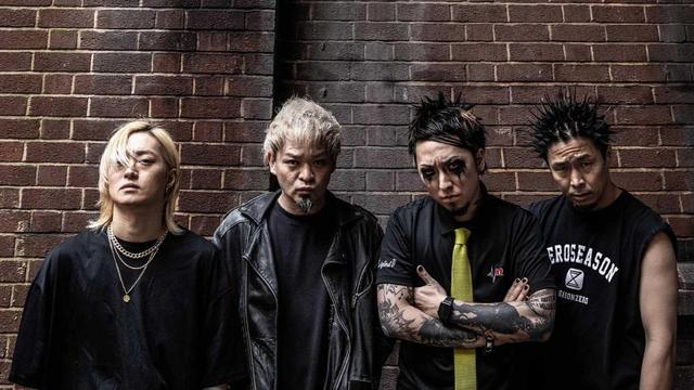 The photo features the four members of the Japanese band SiM (Silence iz Mine), all dressed in black attire and with serious facial expressions, posing in front of a red brick wall. 