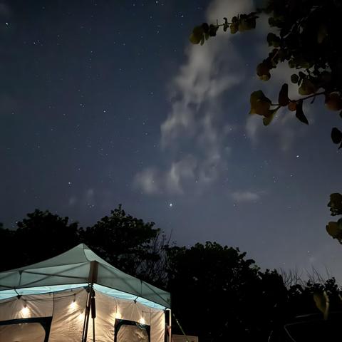 Starry sky above a lighted camp tent.