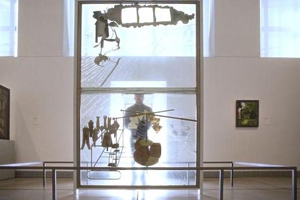 An art installation featuring a partially transparent structure with abstract shapes and figures, set in a gallery space. A person is visible behind the installation, and there are tables in the foreground with artworks on display.
-

The Bride Stripped Bare by Her Bachelors, Even (The Large Glass)
1915-1923  by Marcel duchamo