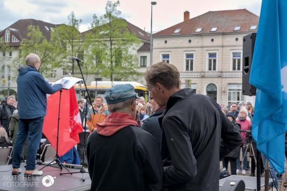 Bernhard Gorka und Udo Frigger reden hinter der Büne, auf der eine Rede gehalten wird