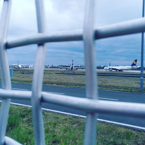 Drei geparkte Flugzeuge der Lufthansa, durch einen Zaun fotografiert.