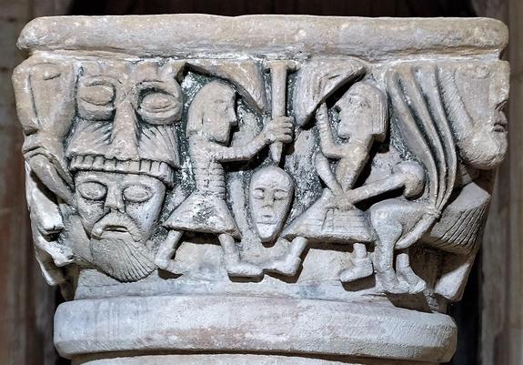 Four sided baptismal font with complex imagery. On this side is a central tableau of two people fighting with shields and axes, plus several faces/masks that apear unrelated.
