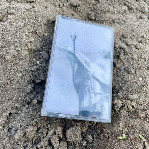 Eine teilweise vergrabene Kassette mit einem Schwarz-Weiß-Bild auf der Hülle, die im trockenen Boden liegt.