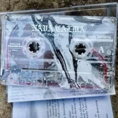 Eine durchsichtige Kassette mit sichtbaren Spulen, beschriftet mit "NAVA CALMA", die auf einer strukturierten Oberfläche neben einem bedruckten Blatt Papier liegt.