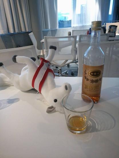 The DrupalCon Vienna mascot stuffed horse lying on its back with an Jaloviina bottle next to it.