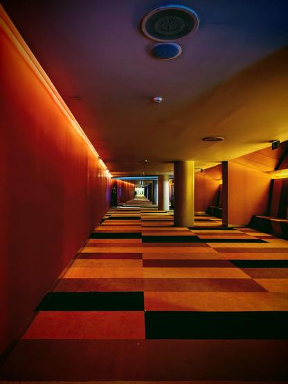 Fotografía vertical con móvil de los pasillos de los cines Aragonia (Zaragoza) que cuentan con un suelo de figuras geométricas en moqueta y unos colores rojizos en las paredes.