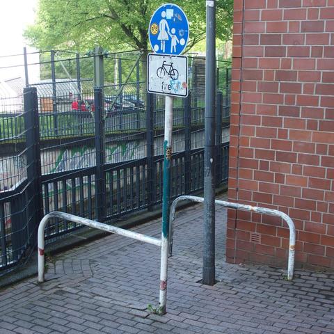 Umlaufsperre mit Z 239 + Radfahrer frei-Schild in Dortmund-Hörde. Der Weg führt zwischen einer U-Bahn-Trasse und einem Wohnhaus vorbei. Relativ mittig in der Umlaufsperre steht eine Laterne.