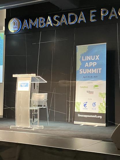 The Linux App Summit 2025 stage, with a podium for the speaker and the conference banner