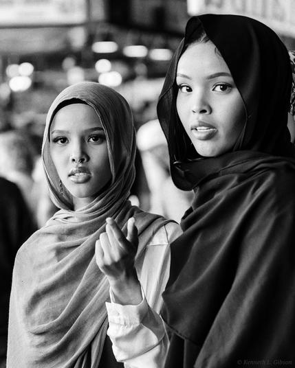 Black and white photo of two women, each wearing a shayla.  One woman is pointing.