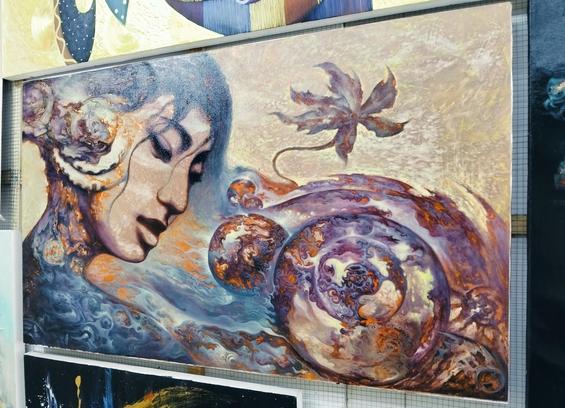 a painting , it is a face seen in a three quarter view with energy and shapes swirling in and around it, there is a wheel of vegetation and energy on the right lower side, a leaf falling above it, the background gold
