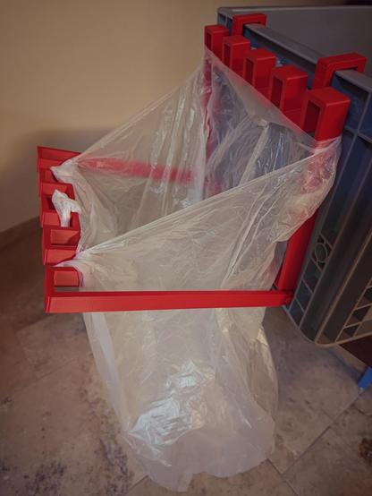 The picture shows a 3D printed trash bag holder made of ASA holding a trash bag.