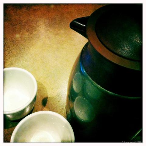 A square image taken with a camera app.  We are looking down on a tea pot, to the right, with two white Chinese tea cups to the left.  The image is artistically colour toned.