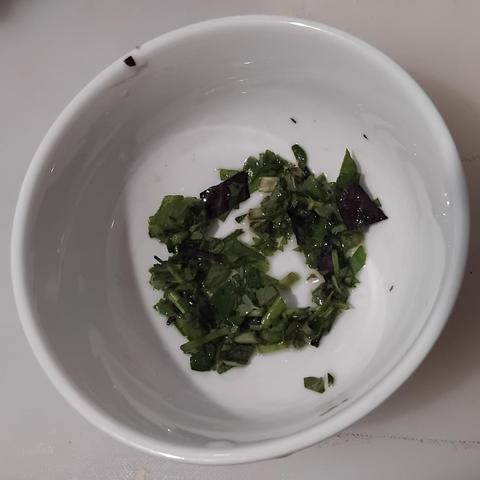 Bowl with small quantity of chopped fresh herbs which are coated in olive oil.