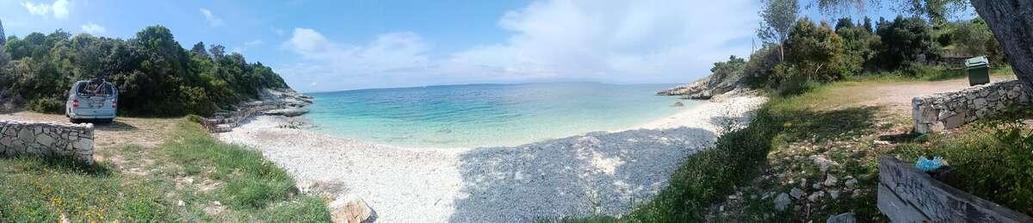 Ein Kiesstrand auf Paxos mit einem blauen VW Bus am linken Rand. 