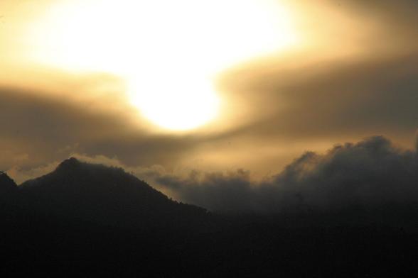 Sunset in the mountains. Sky is coloured yellow and black from the sun and clouds. The hills on the bottom part of the picture are black.