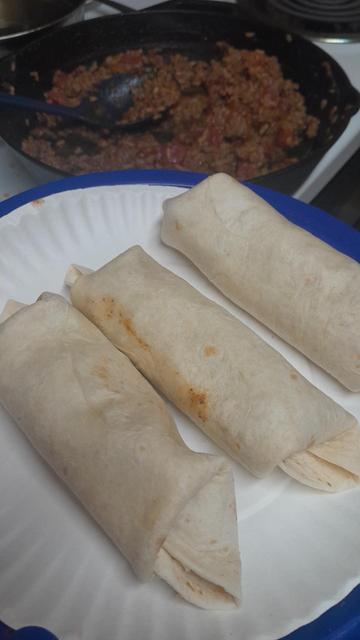 Three very tasty burritos on a plate with a Pan behind it and a lot of mix left