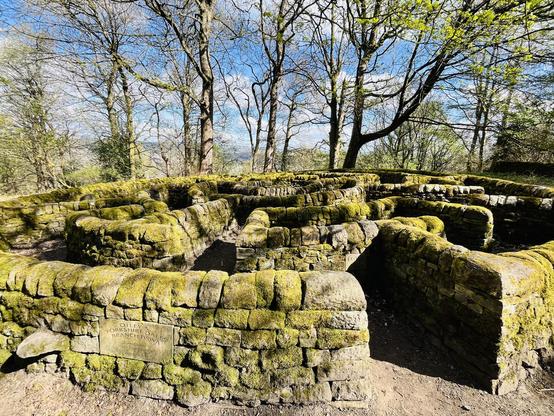 A circular stone maze covered in moss. The picture is taken from just outside the maze looking at the entrance.