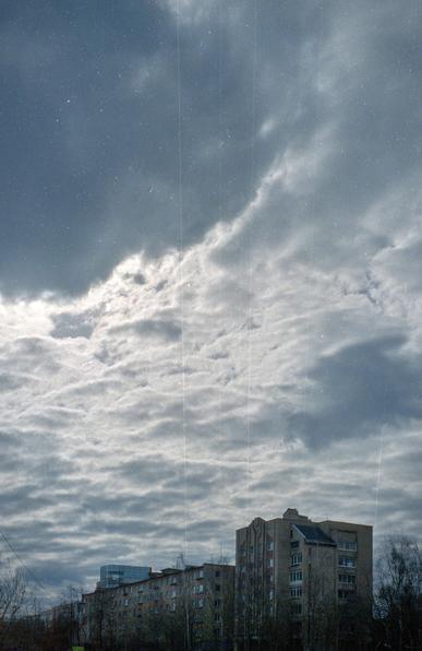 Most of the photo is taken by the sky with clouds behind which the sun is hiding. Several buildings can be seen below. 