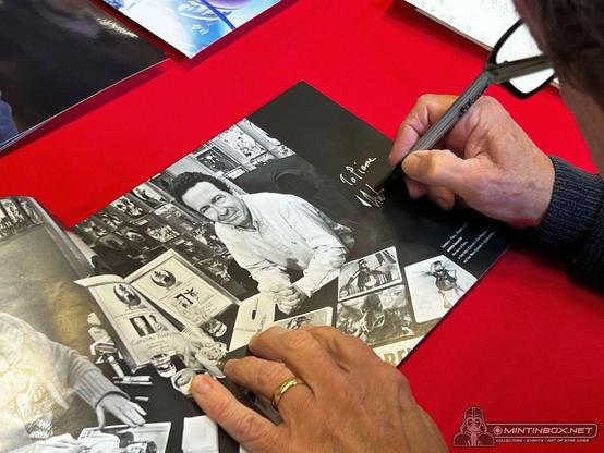 Le livre avec la photo, celle-ci est en noir-et-blanc. On voit deux mains sur la photo, l'une d'elle porte un stylo qui sert à signer la photo.